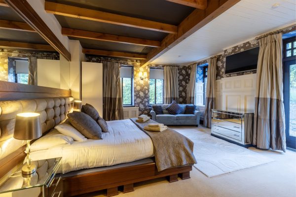 Bedroom under exposed beams with a wall-mounted television and a sofa